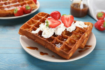 Delicious Belgian waffles with strawberries, whipped cream and caramel sauce on turquoise wooden table, closeup