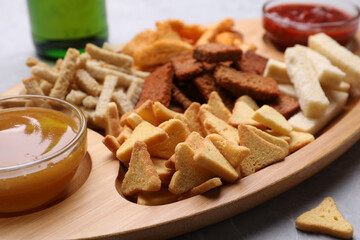 Wooden tray with different crispy rusks and dip sauces on table, closeup