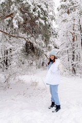 A beautiful young woman in a stylish outfit walks in the forest in winter. Emotions, candid people