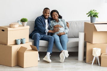 Fototapeta na wymiar Happy Black Pregnant Couple Relaxing On Couch After Moving To New Apartment