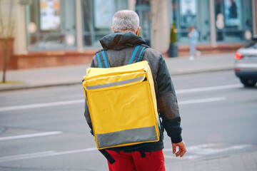 Courier of food deliver service. Food delivery adult man with yellow backpack delivering fast food. Delivery service man with thermal backpack delivering food from restaurant, supermarket or cafe.