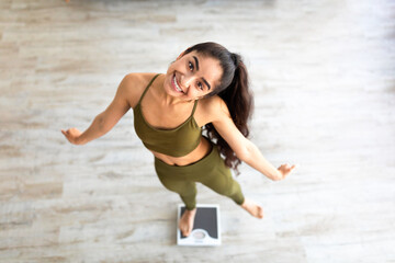 Above view of millennial Indian lady dancing on scales, choosing healthy lifestyle, happy with...