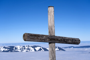 Wooden cross at mountain Fronalpstock at mountain village Stoos on a sunny winter day with sea of...