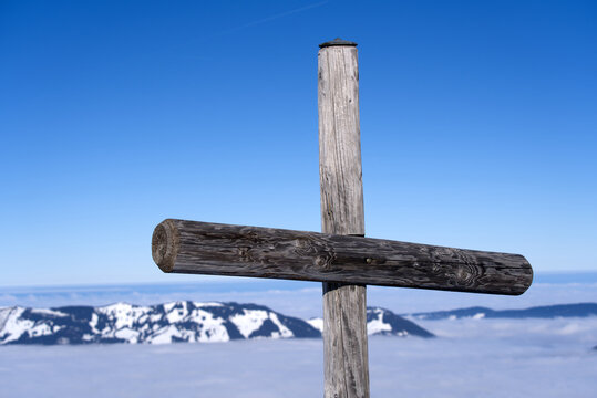 Wooden cross at mountain Fronalpstock at mountain village Stoos on a sunny winter day with sea of fog and mountain panorama. Photo taken December 20th, 2021, Stoos, Switzerland.