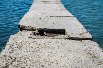 Breakwater extending far out to sea. Concrete slabs of breakwater are destroyed in middle....