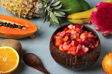 Tropical fruit salad in coconut bowl on a light blue background, Closeup