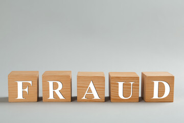 Wooden cubes with word Fraud on grey background, space for text