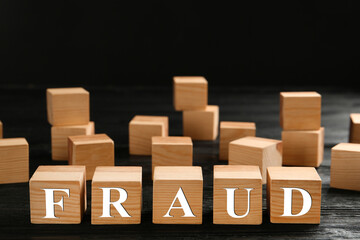 Wooden cubes with word Fraud on black table, space for text