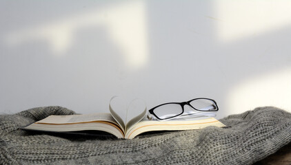 The pages of an open book are folded in the shape of a heart. The book is on the sweater. There are glasses on the book. Concept education