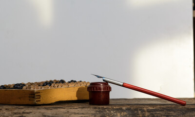 There is an inkwell with a fountain pen on the notebook. Next to the wooden abacus