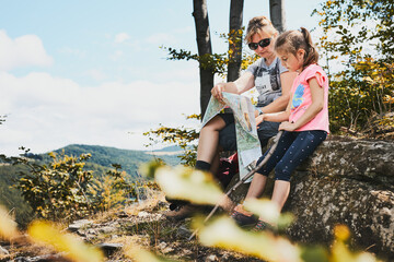 Family trip in mountains. Mother and her daughter examining a map of mountains trials sitting on...