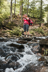 Taking pictures from vacation. Woman with backpack taking photos of landscape using smartphone camera standing on rock on mountain stream during summer trip