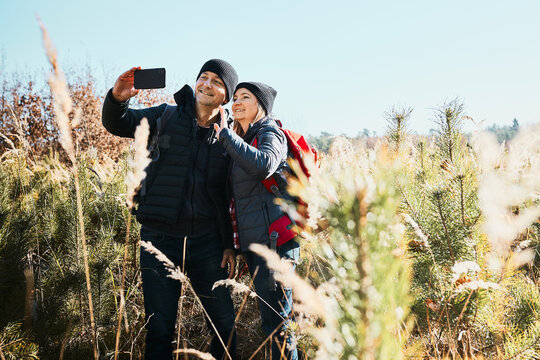 Couple having video call sending greetings from vacation trip. Hikers with backpacks on way to mountains. People walking through tall grass along path in meadow on sunny day