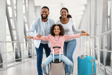 Black family traveling with daughter, having fun in modern airport