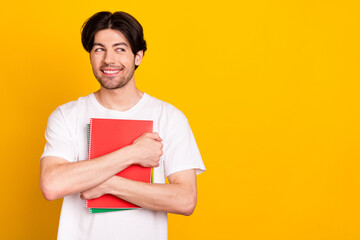 Portrait of attractive cheerful curious guy hugging copybook looking aside copy space isolated over bright yellow color background