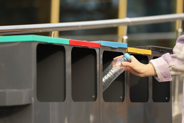 Woman throwing plastic bottle into sorting bin outdoors, closeup