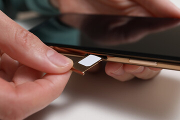 Woman putting SIM card tray in smartphone at white table, closeup