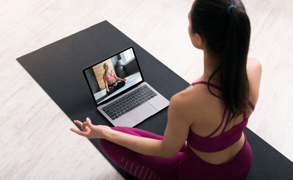 Above view of young woman doing breathing exercises or meditation, following video tutorial on laptop at home