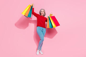 Full length body size view of attractive cheerful grey-haired woman holding bags having fun isolated over pink pastel color background