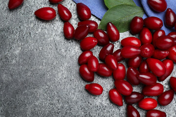 Pile of fresh ripe dogwood berries and green leaves on grey table, flat lay. Space for text