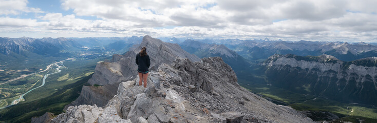 Wide panoramic shot of female hiker enjoying the views on valley from mountain summit