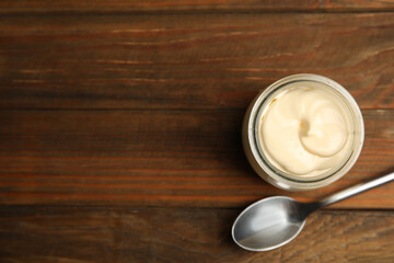 Jar of delicious mayonnaise and spoon on wooden table, flat lay. Space for text