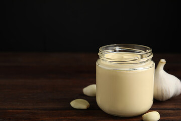 Jar of delicious mayonnaise and fresh garlic on wooden table. Space for text