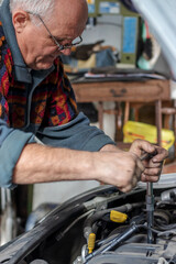 Portrait of a senior car mechanic changing spark plugs on his old car in the garage. Fixing spark plugs with a special long screwdriver. Old car mechanics and repair concept. Manual work.