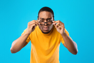 Naklejka premium African American Man Squinting Eyes Looking Through Eyeglasses, Blue Background