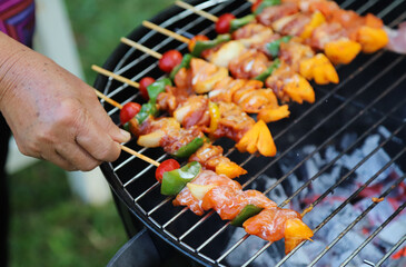 Closeup of  fresh raw  chicken barbecue on gridiron with woman's hand.