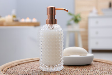Stylish glass dispenser and soap bar on wicker stool in bathroom