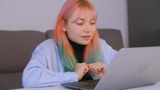Freelancer girl with dyed hair stretching arms and typing text on laptop keyboard. Young woman with colored hair doing distant free lance work during lockdown
