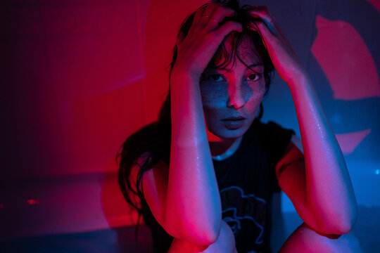 Portrait in red neon light of young depressed asian woman suffering from alcohol or drug addiction, sitting in dark bathroom at home, having substance abuse problem. Depression and mental health