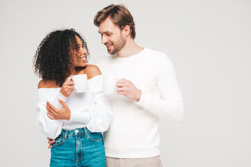 Smiling beautiful woman and her handsome boyfriend. Happy cheerful multiracial family having tender moments on grey background  in studio. Multiethnic models hugging. Drinking tea. Holding cup