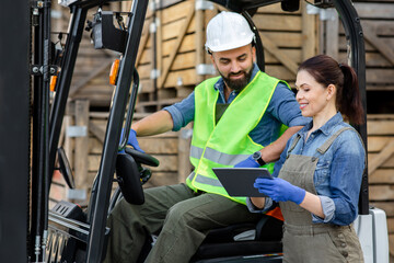 Millennial bearded man in helmet in forklift truck, discussing order with smiling woman