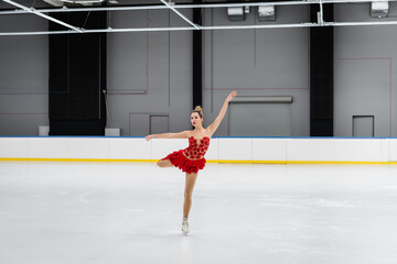full length of figure skater in red dress performing camel spin in ice arena © LIGHTFIELD STUDIOS