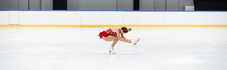full length of young woman in dress performing sit spin in professional ice arena, banner - obrazy, fototapety, plakaty