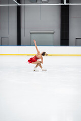full length of young woman with outstretched hand figure skating in professional ice arena