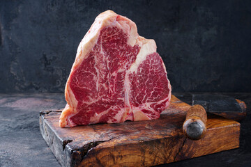 Raw dry aged wagyu porterhouse beef steak offered as close-up on rustic old wooden board with a...