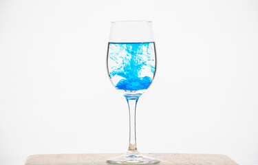 Blue food coloring is spread in water in a wine glass.