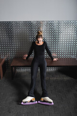 full length of young woman in white figure skates stretching near bench