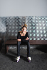 full length of young woman in white figure skates and black bodysuit sitting on bench