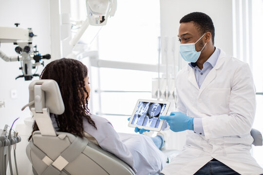 Male Black Dentist Doctor Demonstrating Female Patient Teeth Xray On Digital Tablet