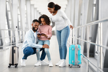 Happy excited black family traveling, looking at documents in airport