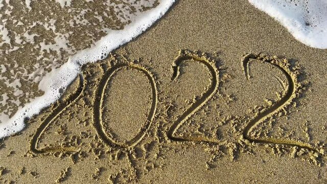 The word 2022 written on the sand of the beach is washed away by the sea wave. The surf on the beach washes away the word