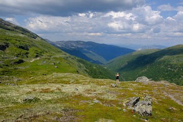 Fototapeta premium Landscape of plateau around National Tourist Route Aurlandsfjellet, known locally as the Snow Road (Snøvegen). Silhouette of walking young woman on plateau. Norway