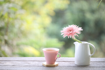 Pink cup and pink gerbera flower on wooden table