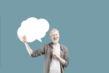 Excited young albino man pointing at empty speech bubble, standing over blue studio background, mockup for design