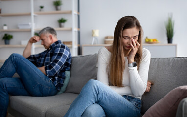 Unhappy mature woman wiping tears from her eyes on couch after conflict with her husband at home, empty space