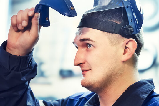 Portrait Of Metalworker Or Worker. Young Caucasian Looks From Under Visor Of Protective Mask. Real Worker In Workshop. Close-up. Face Portrait.